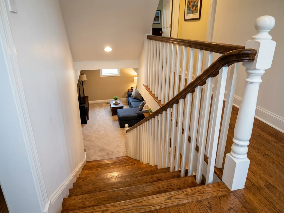 Basement stairway opened on one side with white painted balusters, a wood handrail and oak treads leading down to a finished room
